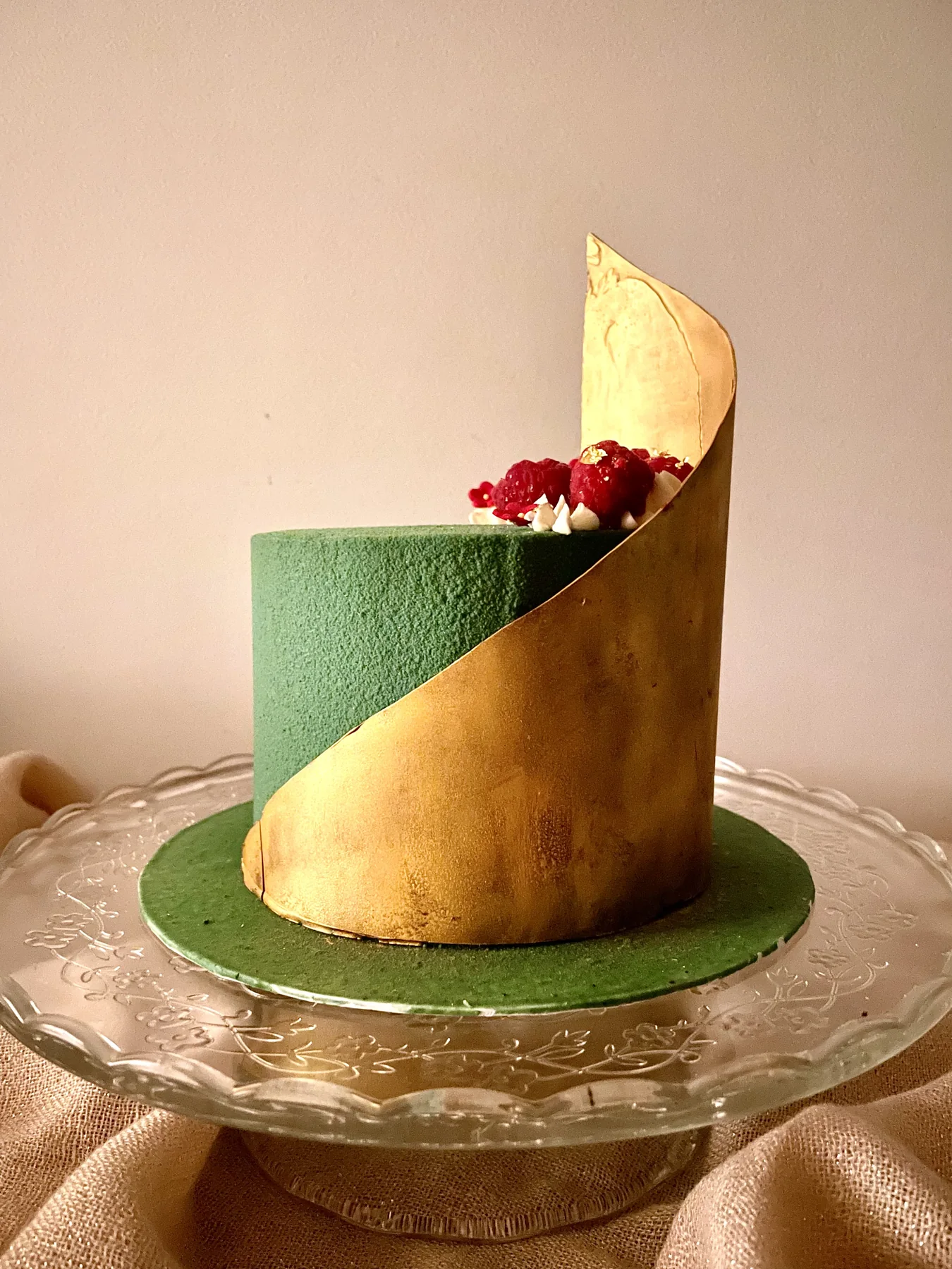 Forest-green velvet cake with a sweeping gold leaf panel and fresh red berries