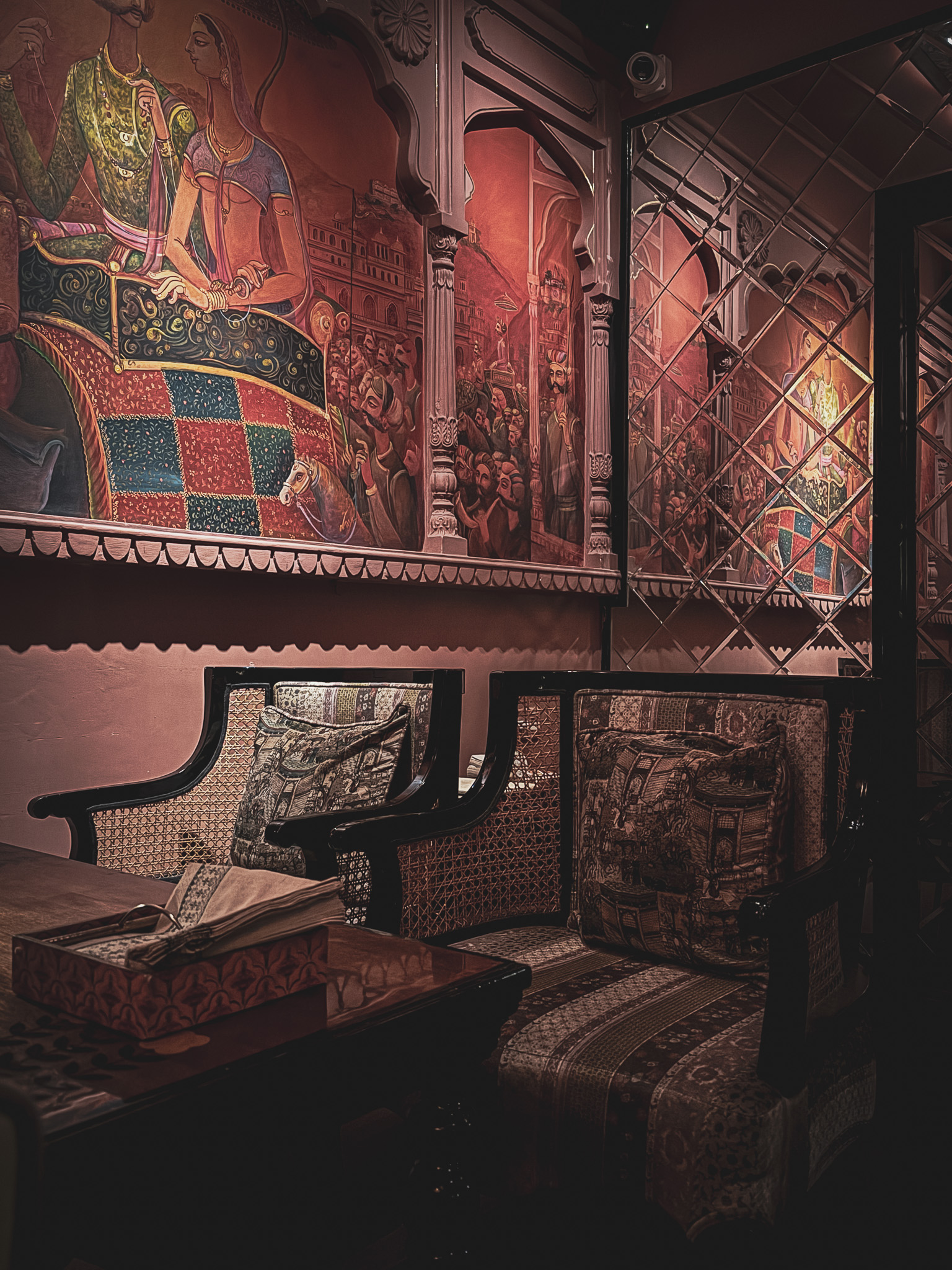 Dark intimate alcove with hand-painted Rajasthani murals and carved cane seating