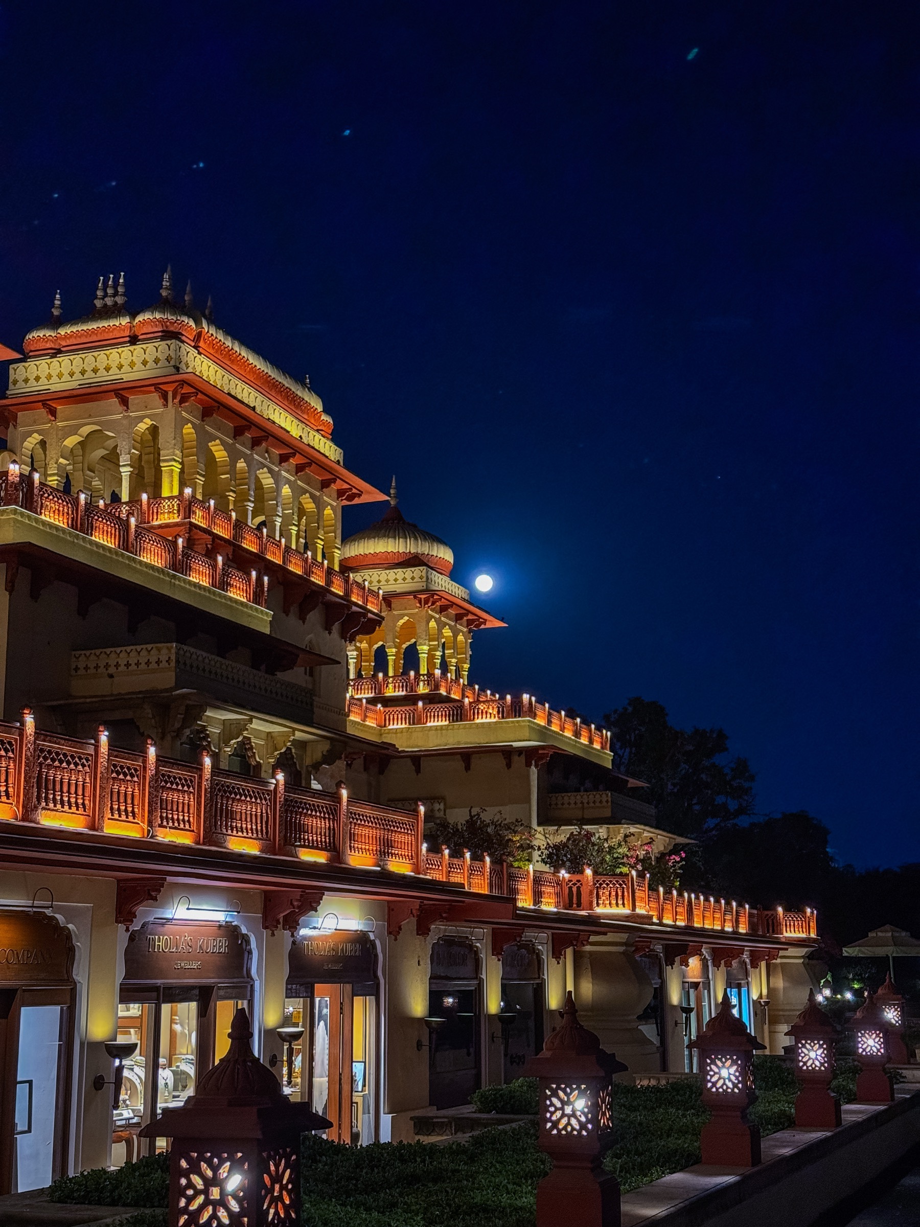 Illuminated Rajasthani palace facade at night with a full moon rising behind