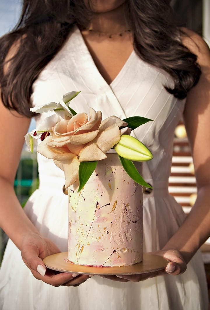 Hands presenting a hat-box cake crowned with an oversized sugar rose